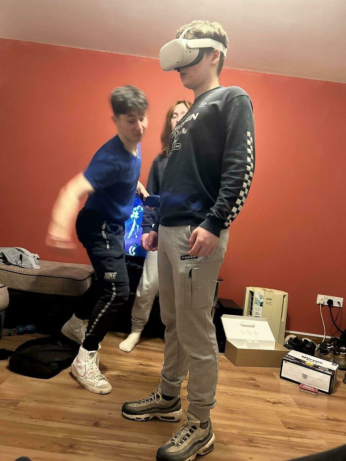 Three teens in a room with one wearing a VR headset, capturing a frozen frame that tells everything without showing aftermath.