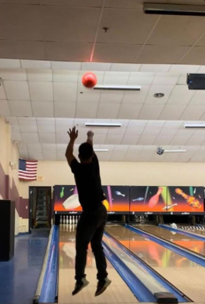 Person in mid-air throwing a red bowling ball in a frozen frame capturing the action without showing aftermath.