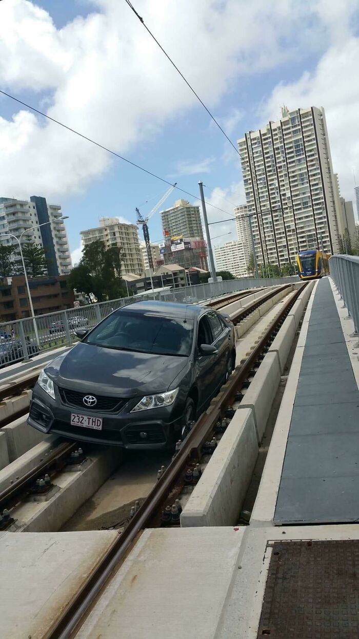 Black car stuck on tram tracks in an urban setting, a frozen frame capturing unexpected moments on city rails.