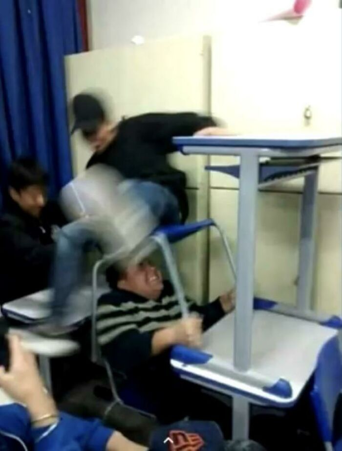 Young men caught in a frozen frame, one falling over a chair in a chaotic and blurred action moment indoors.
