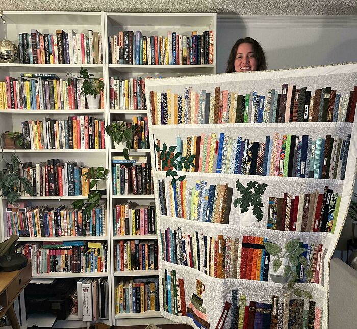 Person holding a creative quilt designed to look like books on shelves, showcasing unique artistic projects.