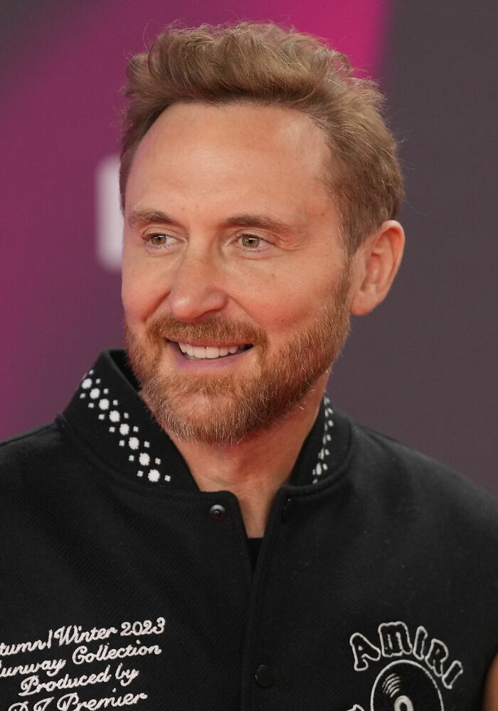David Guetta smiling at an event, wearing a black jacket with white text, showcasing his career highlights.