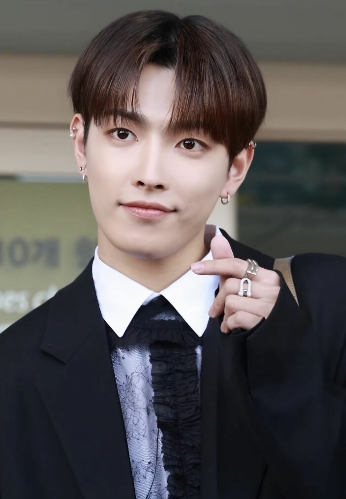 Hongjoong posing outdoors in a black suit and patterned shirt, showcasing his style and career highlights in music.