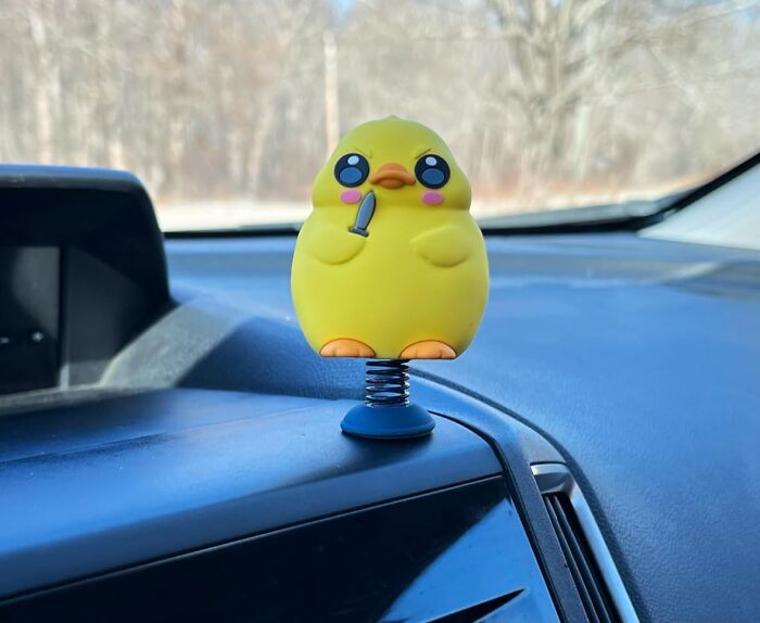 Yellow novelty chick figurine with a tiny knife on a car dashboard spring base, a completely unnecessary novelty find.