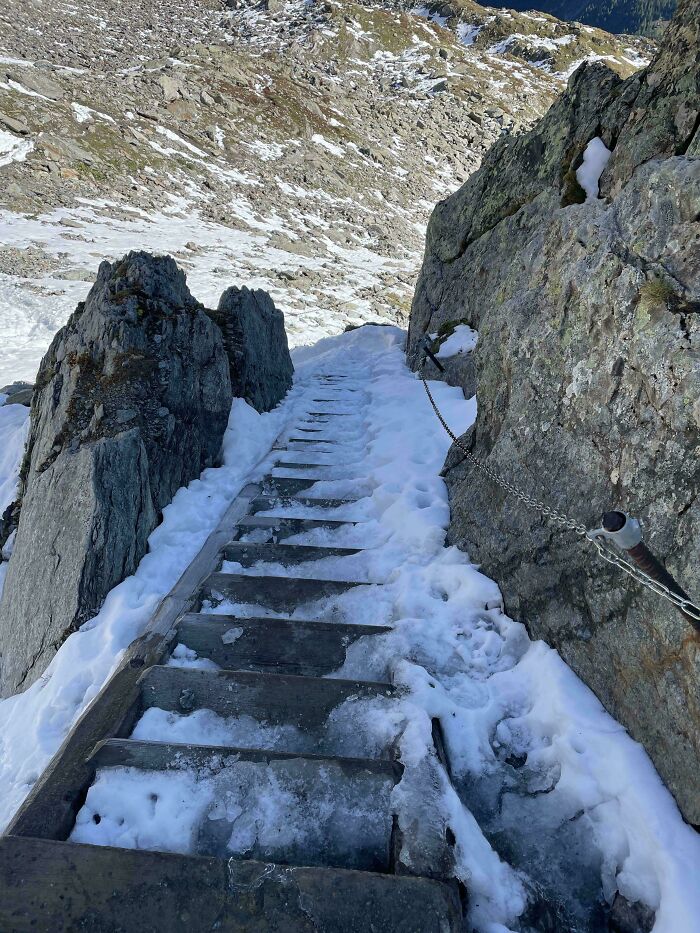 Snow-covered icy wooden stairs with a safety chain on rocky mountain terrain, highlighting Airbnb insanity stairs risk.
