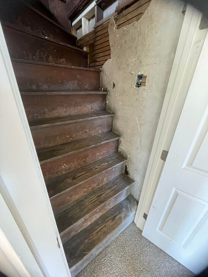 Worn wooden stairs with uneven steps inside a narrow, unfinished wall space needing Airbnb insurance caution.