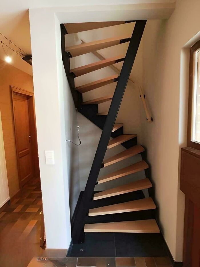 Narrow spiral staircase with wooden steps and black metal frame in a compact modern interior space.