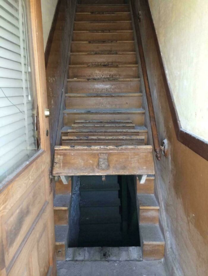 Steep wooden stairs with a hatch door halfway down, illustrating Airbnb insanity requiring stair insurance precautions.