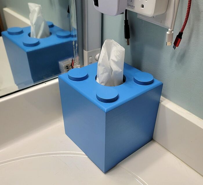 Blue novelty tissue box shaped like a giant building block sitting on a bathroom counter near a mirror and wall outlet.