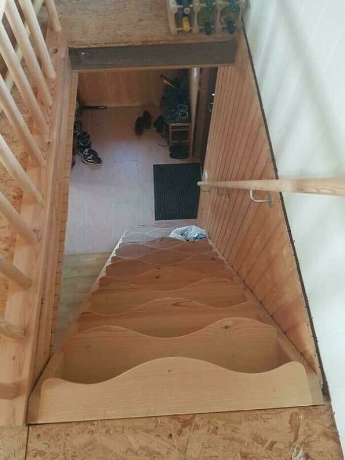 Steep narrow wooden stairs with a railing leading down to an entryway filled with shoes in an Airbnb rental.