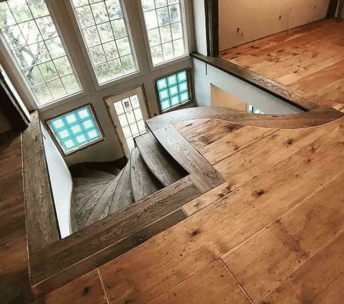 Wooden spiral stairs inside a home with large windows, highlighting Airbnb insanity and the need for insurance.