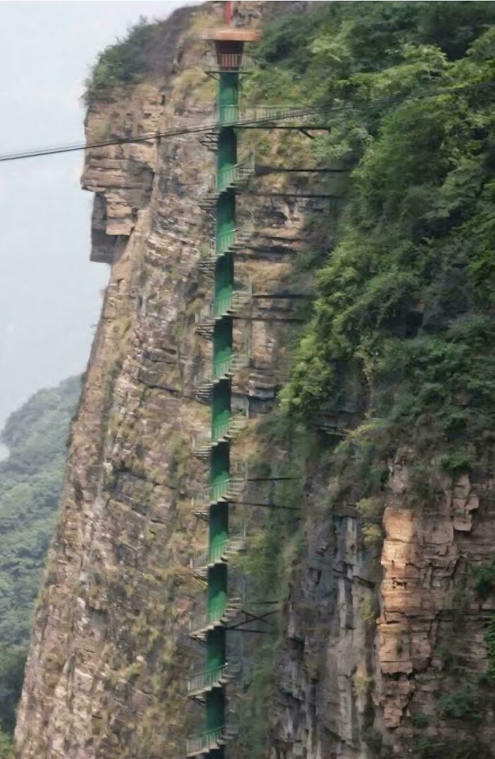 Steep narrow staircase attached to cliffside surrounded by trees, illustrating extreme Airbnb stairs challenge.