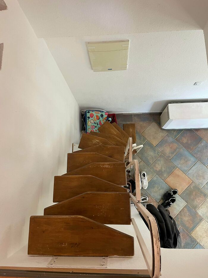 Narrow wooden spiral stairs with worn steps descending to a tiled floor in an Airbnb rental space.