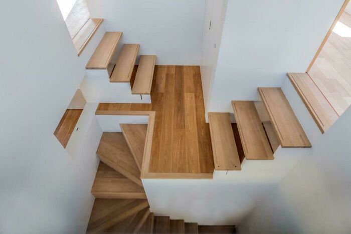 Modern wooden stairs with multiple flights and turns inside a white-walled space, illustrating Airbnb insanity staircase concept.