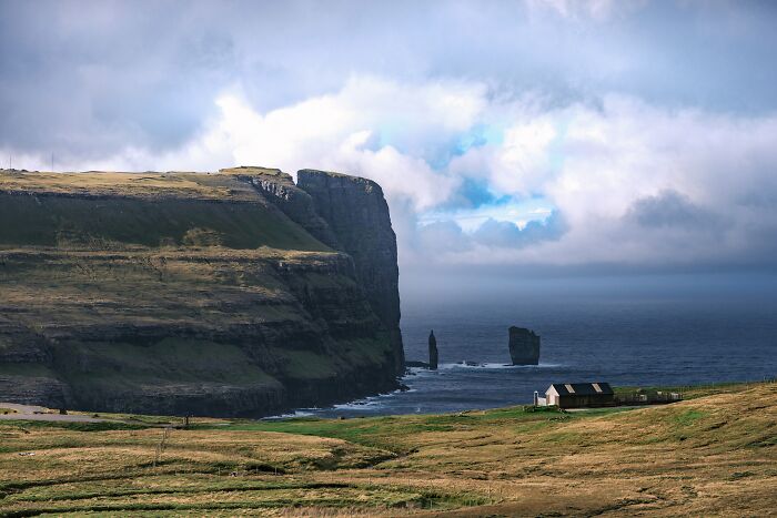 Remote location showing dramatic coastal cliffs, ocean, and a small house under a cloudy sky in a mind-blowing setting