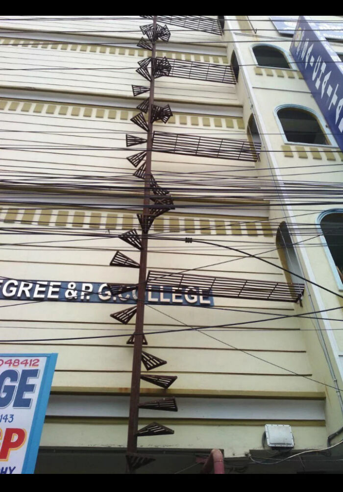 Rusty narrow spiral staircase on a building exterior tangled with numerous black electrical wires for Airbnb insurance caution.