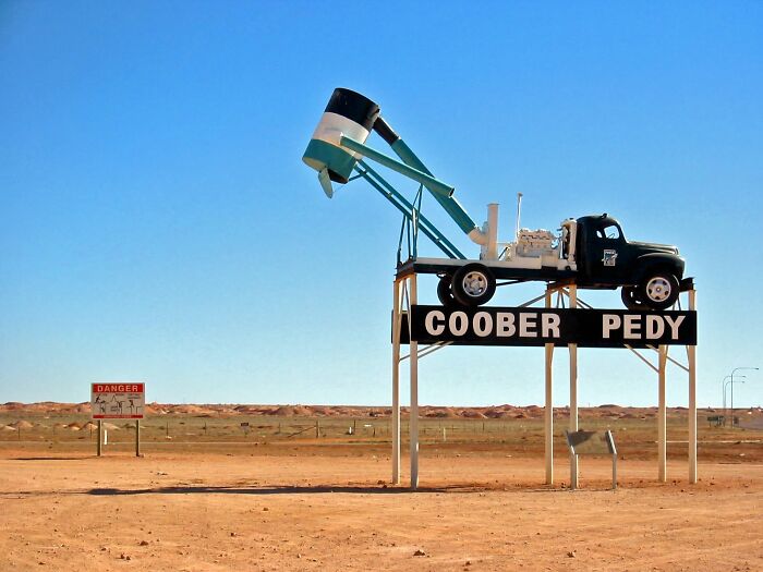 Coober Pedy sign with mining truck sculpture in a remote location under a clear blue sky in the arid desert landscape.