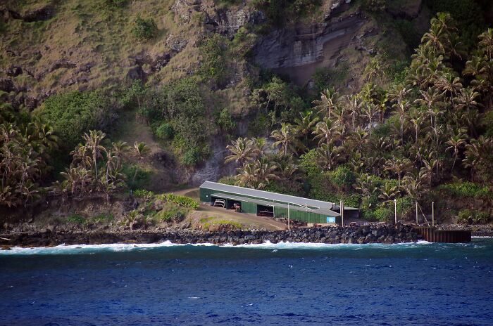 Remote location with a green building, surrounded by palm trees and cliffs near the ocean shore.