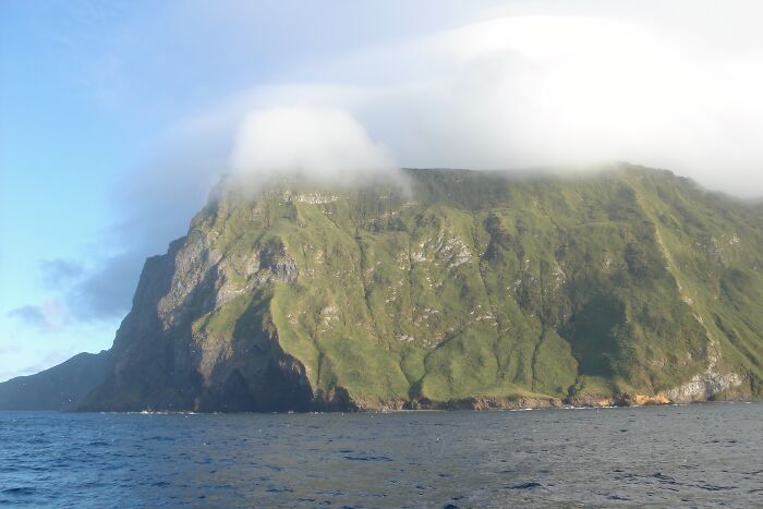 Remote location with lush green cliffs partially covered by mist and surrounded by ocean under a clear sky.