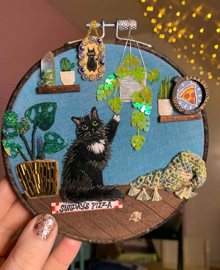 Embroidered artwork of a black cat reaching for hanging plant leaves, showcasing creative projects and detailed craftsmanship.