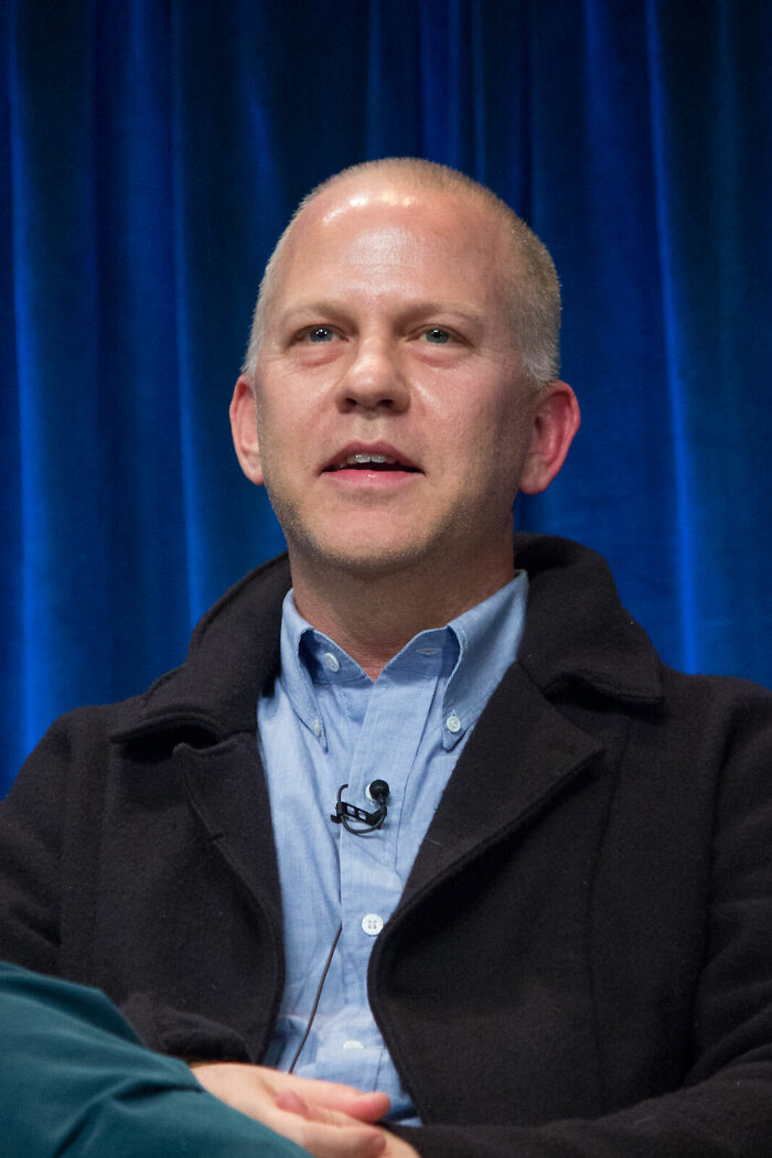 Ryan Murphy speaking at an event, wearing a blue shirt and black jacket with a microphone attached.