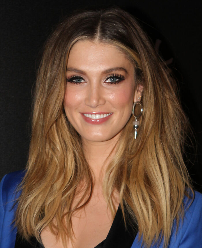 Delta Goodrem smiling with long blonde hair and hoop earrings, showcasing her bio and career highlights in entertainment.