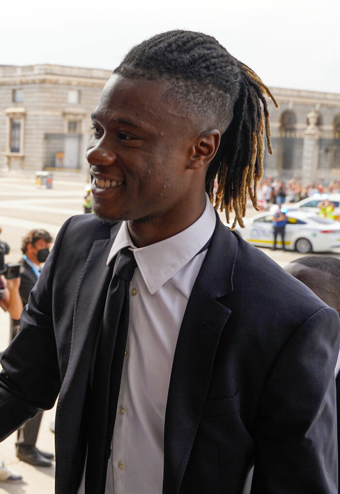 Eduardo Camavinga smiling outdoors in a black suit and tie, engaged with fans at a public event.