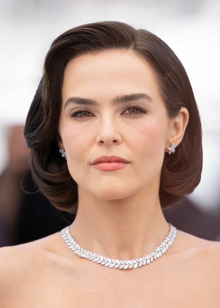 Zoey Deutch wearing a diamond necklace and earrings with styled hair at a formal event, showcasing her career highlights.