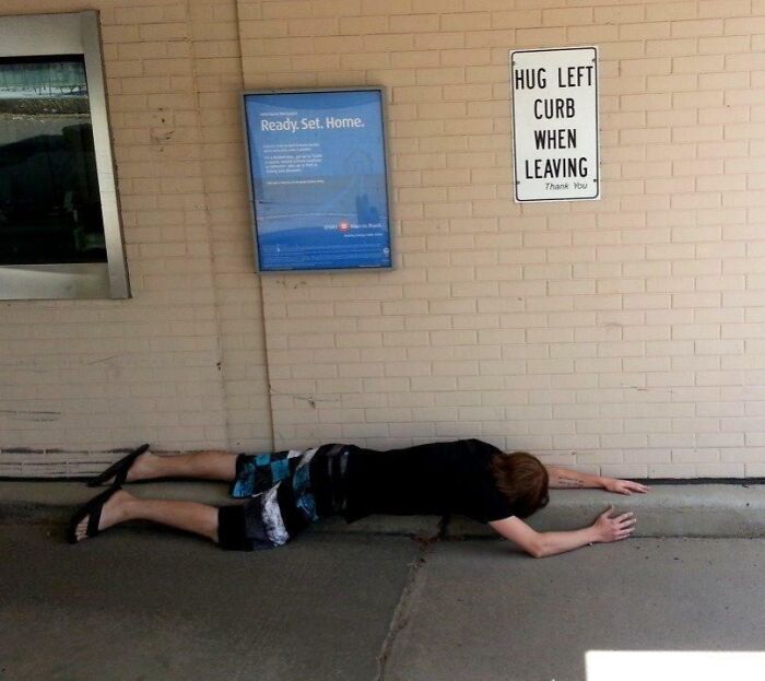 Person lying flat hugging the left curb exactly as instructed on a sign, showcasing unhinged pics of people doing tasks.