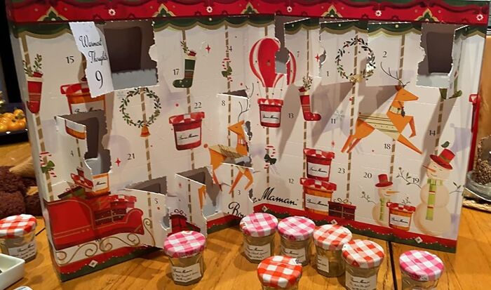 Advent calendar with numbered doors open, featuring holiday illustrations and small jars on a wooden table for Christmas countdown.