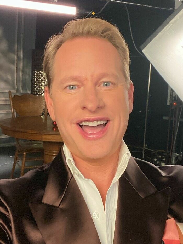 Carson Kressley smiling in a dark suit jacket and white shirt, posing for a close-up photo indoors.