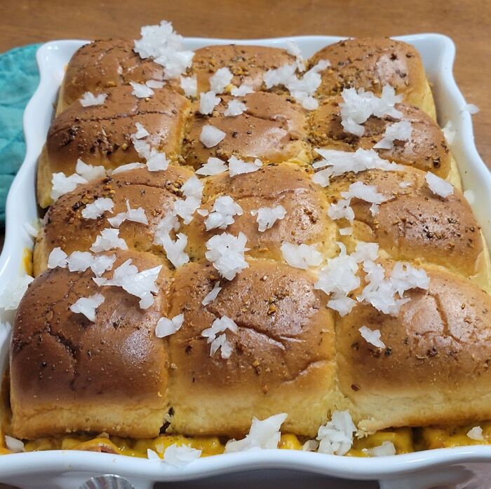 Baked dinner rolls topped with chopped onions in a white baking dish, showing a family cooking moment.