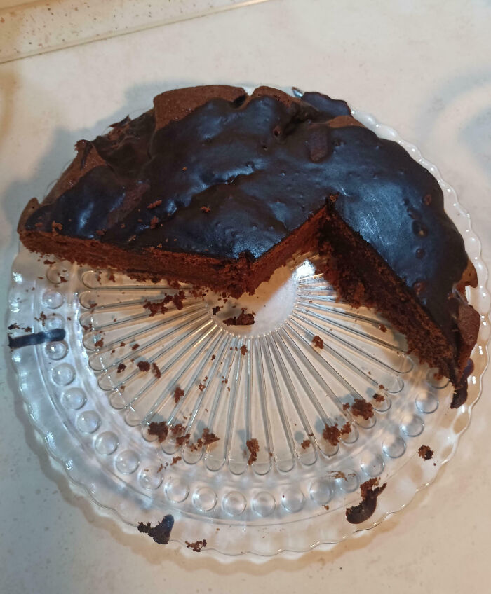 Partially eaten chocolate cake with uneven slices on a clear glass plate, showcasing family member frustration moments.