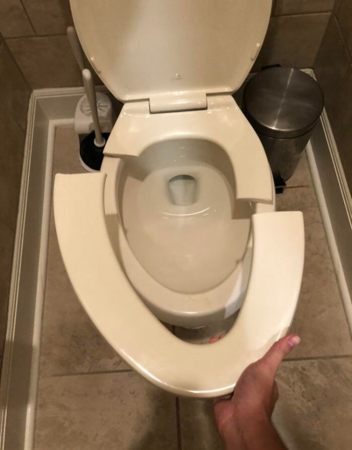 Hand holding a broken toilet seat in a bathroom, showing family members' infuriating behavior vented online.