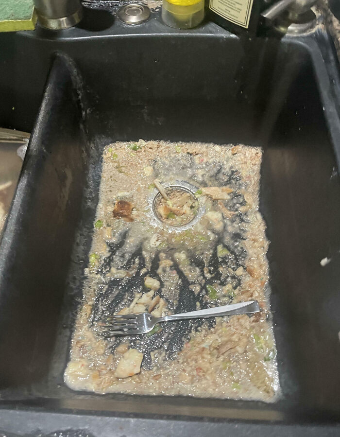 Dirty kitchen sink clogged with food scraps and a fork, showing frustration with family members' messes online.