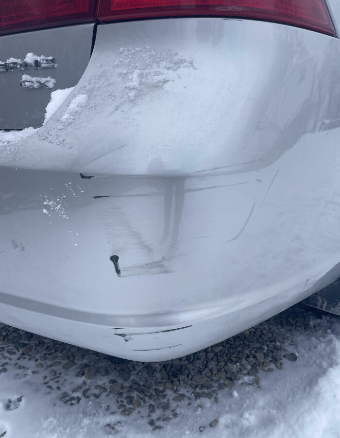 Scratches and damage on a white car bumper in a snowy area, highlighting family members' infuriating actions shared online.