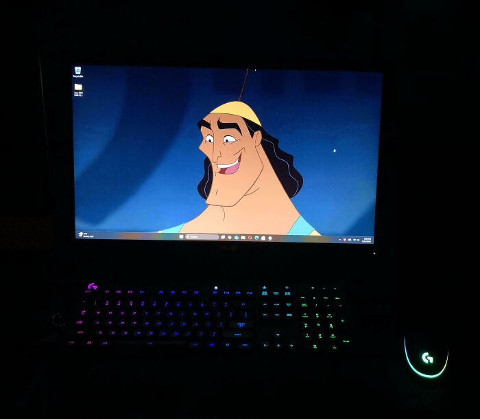 Computer screen with animated character as desktop background, illuminated gaming keyboard and mouse in dark room.