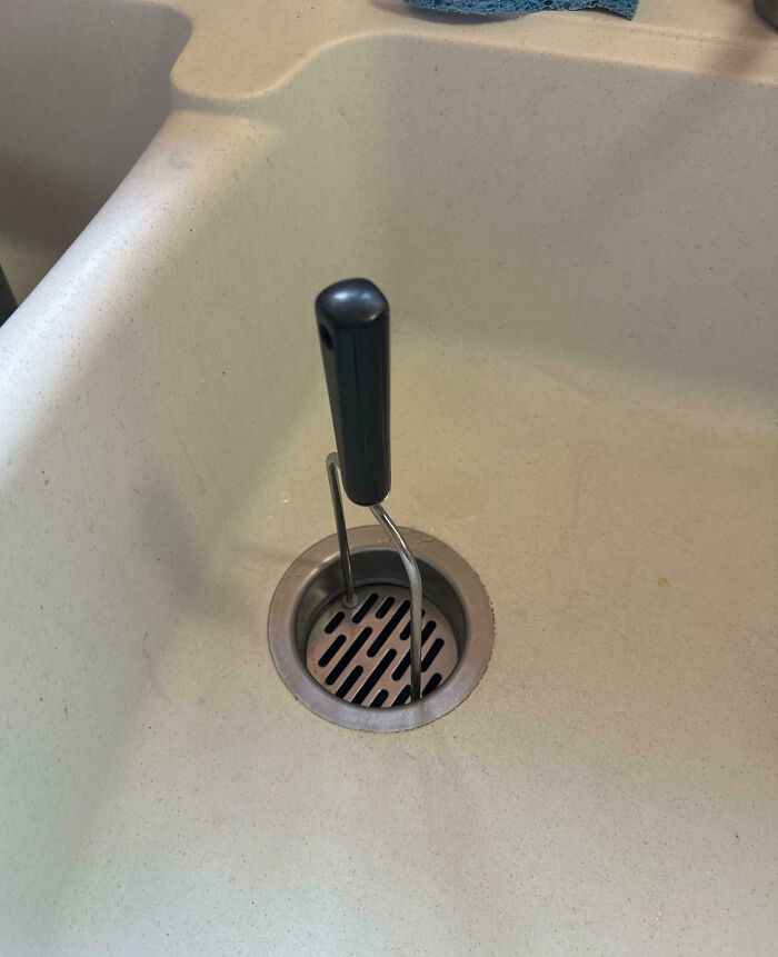 Black handled potato masher stuck in a kitchen sink drain, illustrating frustration with family members in a humorous way.