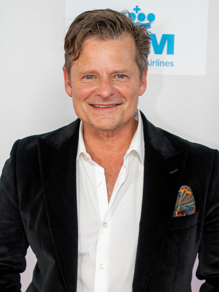 Steve Zahn smiling in a black blazer and white shirt at a media event, highlighting his bio and career.