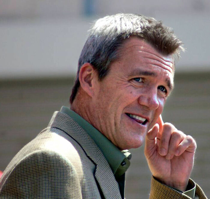 Neil Flynn smiling outdoors, wearing a brown checkered jacket and green shirt, highlighting his career and bio.