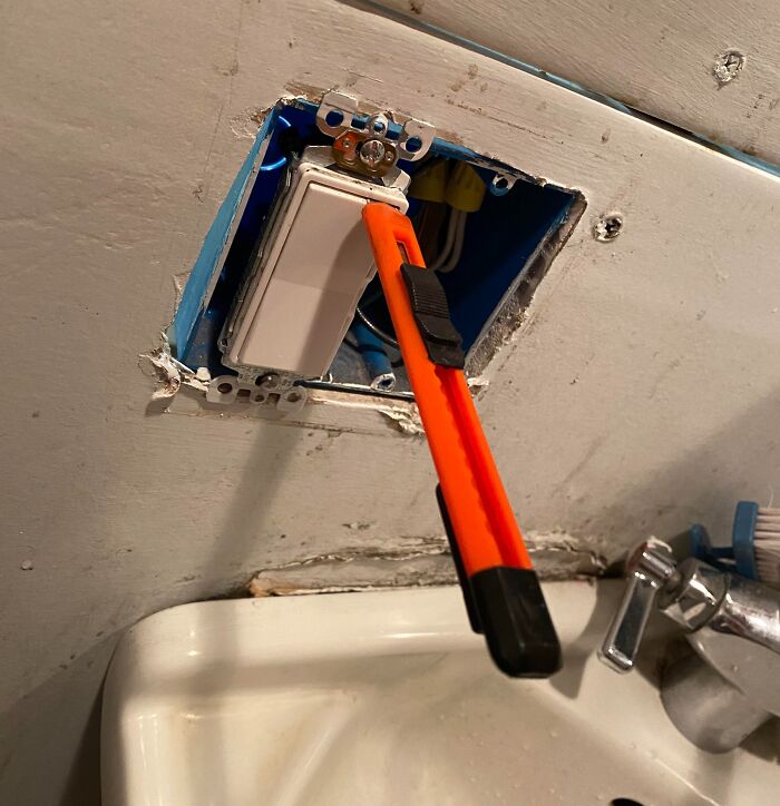 Utility knife wedged into a light switch box as a makeshift tool showing people not even trying at work.