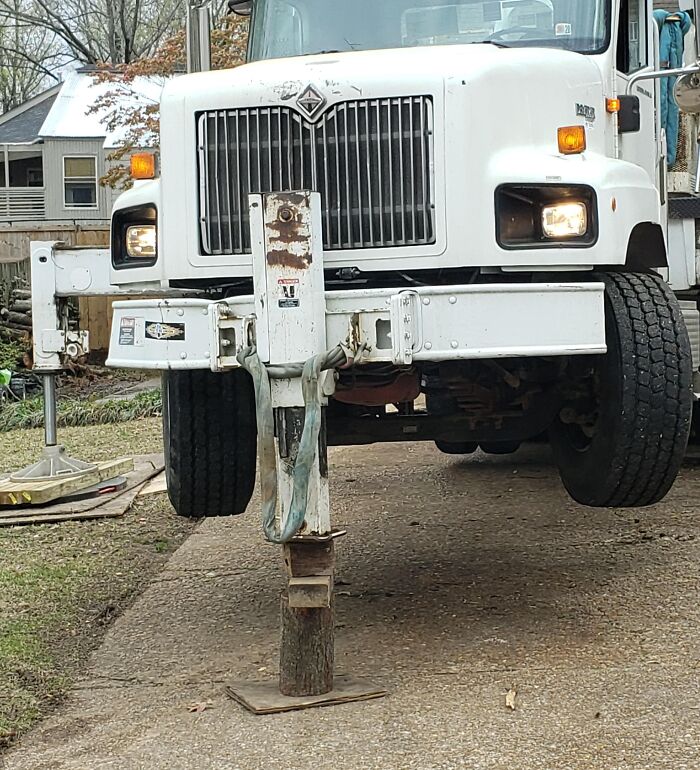 White truck improperly stabilized on wooden log on driveway, a funny example of people not even trying at their job.
