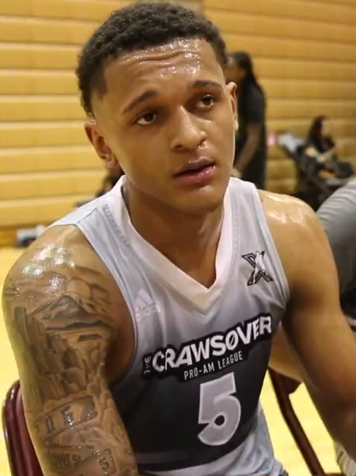 Paolo Banchero sitting in basketball uniform with visible arm tattoo, sweaty after a game in an indoor gym.