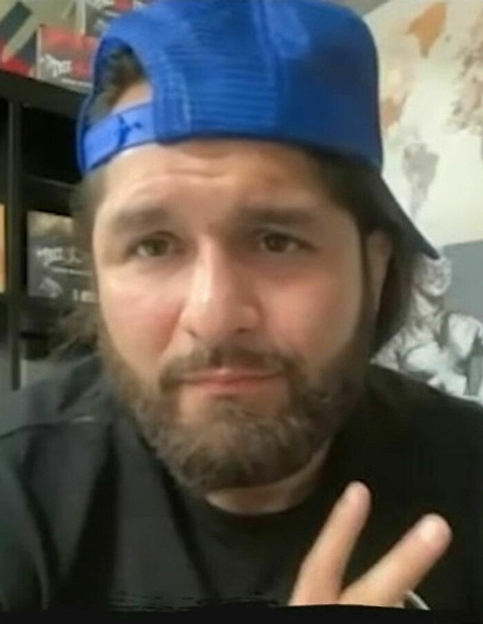 Jorge Masvidal wearing a blue backward cap and showing a peace sign with a casual expression indoors.