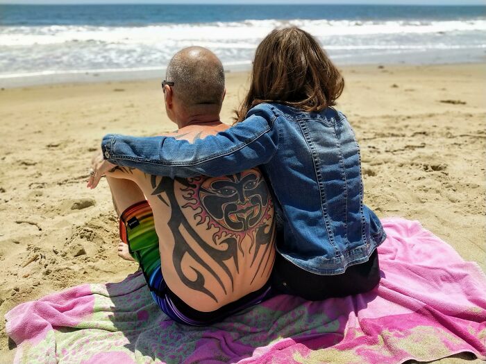 Two siblings sitting together on a beach towel by the ocean, showing gratitude and closeness at the seaside.