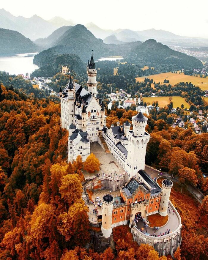 Aerial view of a historic castle surrounded by autumn trees and mountains, showcasing an amazing world perspective.