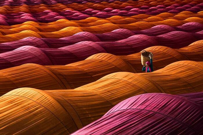 Colorful fabric waves spread across the landscape with a person carrying a basket, showcasing a different perspective of our world.