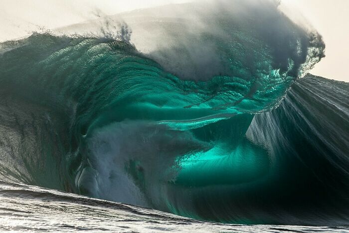 Massive ocean wave curling with sunlight illuminating the water, showing our world from a different perspective.