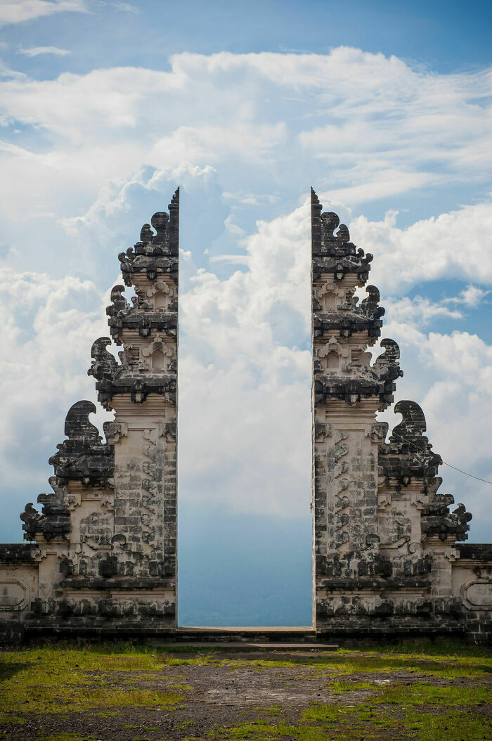 Ancient stone gate with intricate carvings framed against cloudy sky, showing our world from a different perspective.
