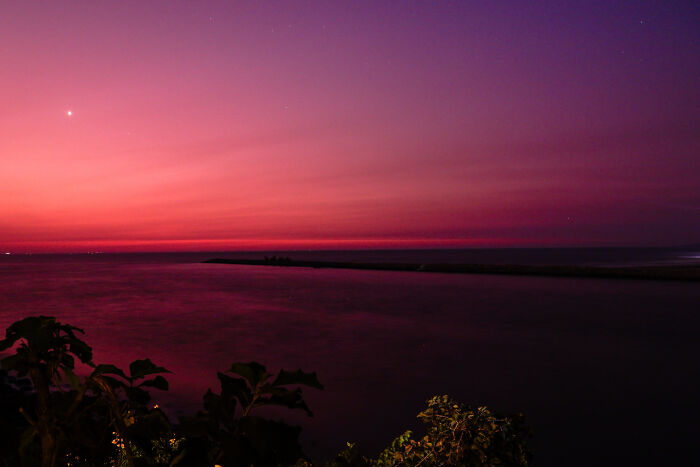 Sunset over calm water with vibrant pink and purple sky, showing our world from a different perspective.